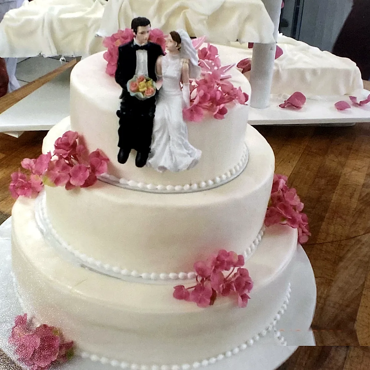Dreistöckige Hochzeitstorte mit Brautpaar und rosa Blüten