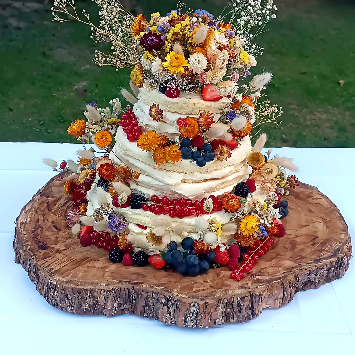 Naked Cake mit Beeren und essbaren Blüten auf einer Holzscheibe